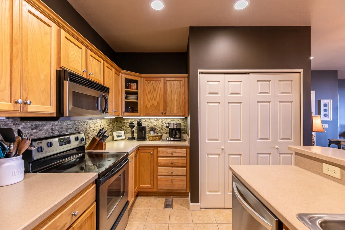 A close-up view of the kitchen area highlighting wooden cabinetry, sparkling stainless steel appliances, clean countertops, and a visible coffee maker. The space is well-lit and organized, making it easy to imagine preparing meals or brewing a fresh cup of coffee.