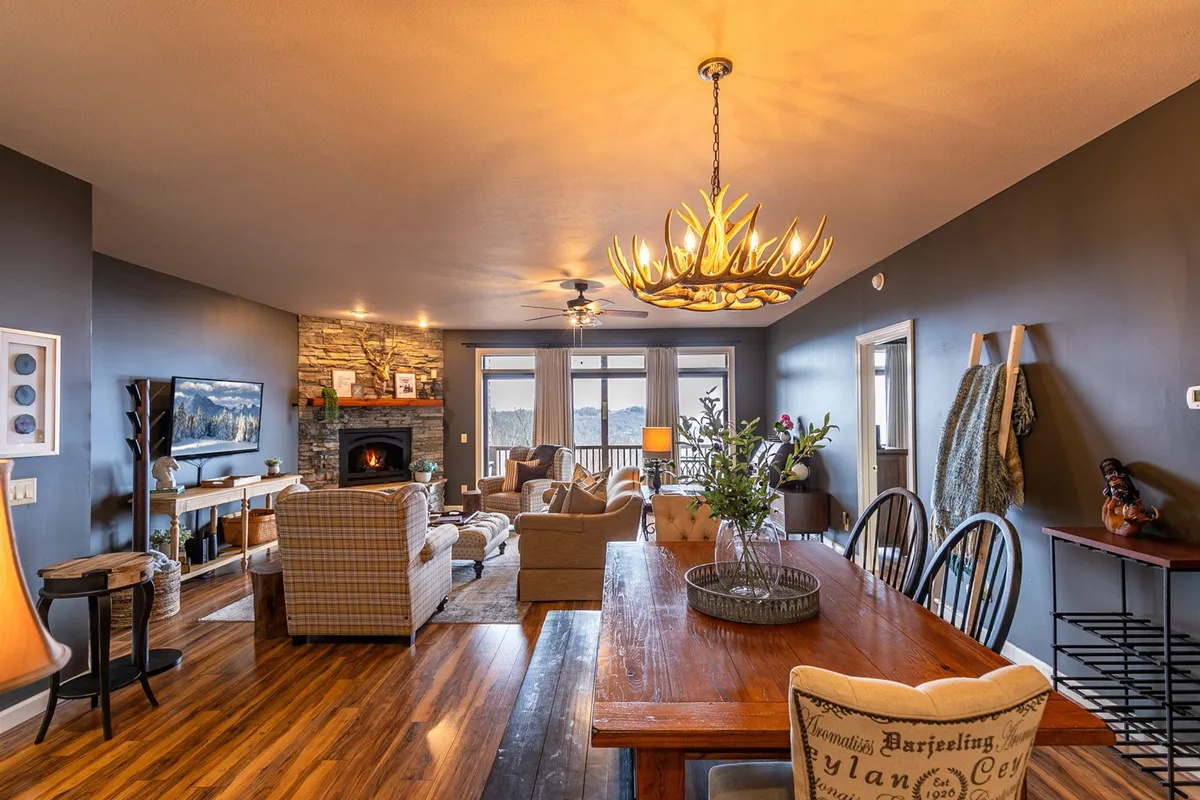 A cozy, inviting living area features a glowing fireplace, a stylish chandelier above the dining table, and a plush sofa, all set against a warm, rustic interior. The space feels perfect for intimate gatherings or unwinding together after a day of exploring.
