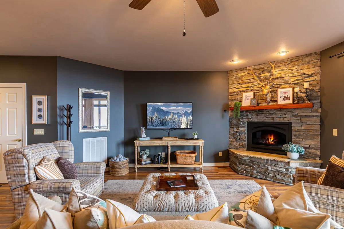 A welcoming living area featuring a stone fireplace, plush seating, a TV, and a window offering glimpses of the surrounding mountains. The space is set up for family gatherings, movie nights, and warming up by the fire after outdoor adventures.