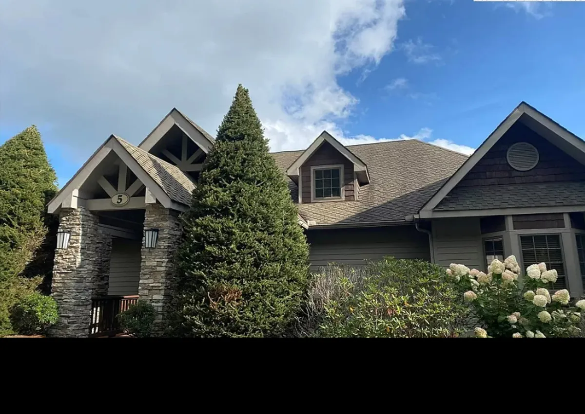 This exterior image captures the stone façade of Sugar Shack, featuring dormer windows, landscaped shrubs, and warmly lit entryway lights. The short stairway leading to the entry is subtly visible, hinting at the approach guests take as they first arrive at the property.