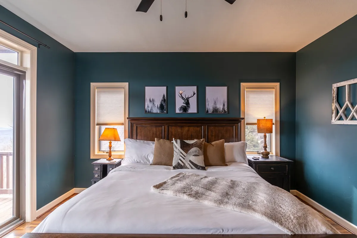 This image showcases a spacious bedroom featuring a large bed with a wooden headboard, decorative pillows, and soft lighting from bedside lamps. Artwork on the wall and warm natural light create a tranquil, inviting vibe, suggesting a restful start or end to a day spent exploring.