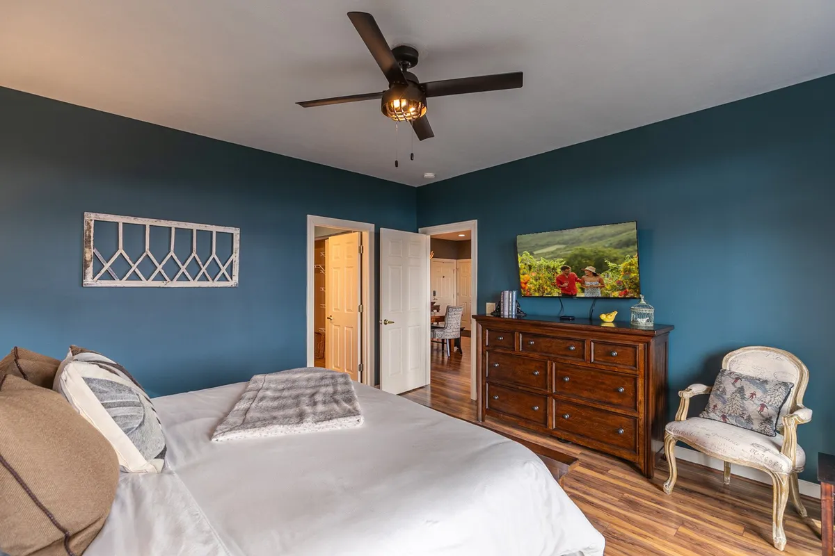 A cozy bedroom scene with a comfortable bed, dresser, wall art, and a plush chair. The ambiance emphasizes warmth and relaxation—perfect for unwinding with a movie night or enjoying quiet moments after a day out.