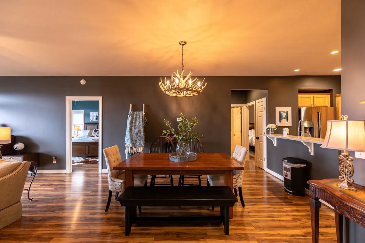 A cozy dining area illuminated by a charming chandelier, with a large table surrounded by comfortable seating and decorative accents. The space is set up for groups to enjoy meals, share stories, and create lasting memories.