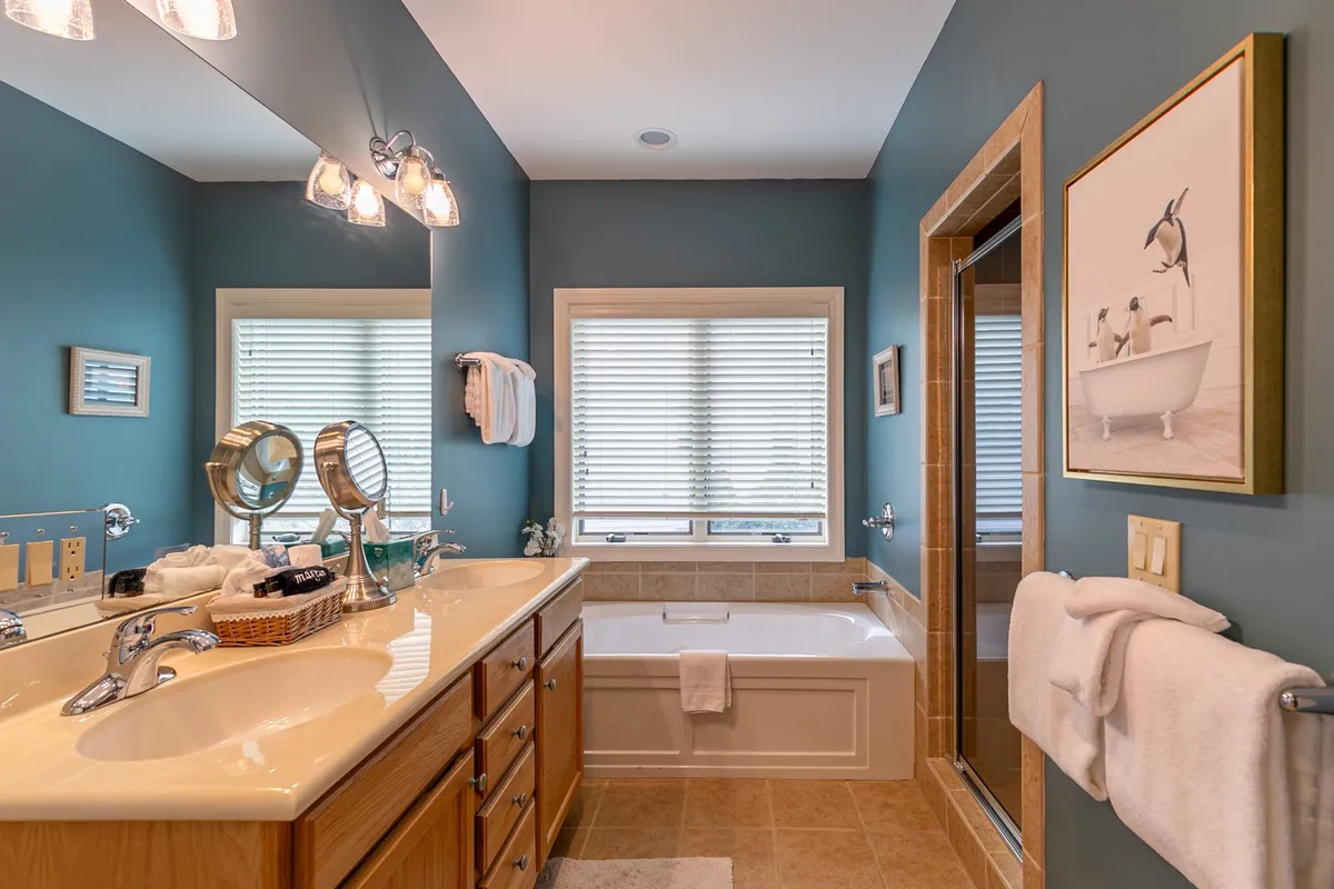 A modern, inviting bathroom with a double vanity, bathtub, glass-enclosed shower, and framed penguin artwork. The space is designed for relaxation and self-care, emphasizing privacy and luxury.