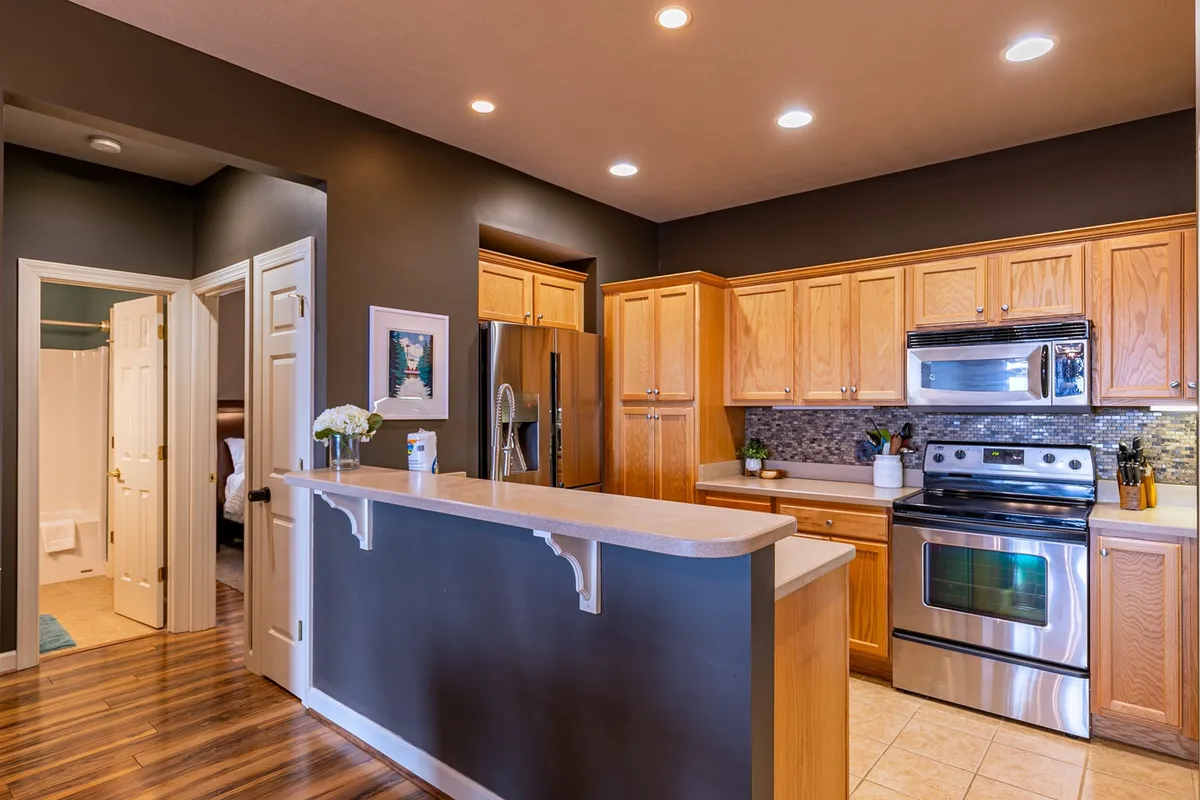 This image showcases a modern kitchen featuring a central island, stainless steel appliances, warm wood cabinetry, and a decorative backsplash. The space is clearly set up for both cooking and entertaining, suggesting a functional yet inviting atmosphere. The layout and elements provide a sense of readiness for culinary adventures, aligning with the section’s emphasis on a fully equipped kitchen.