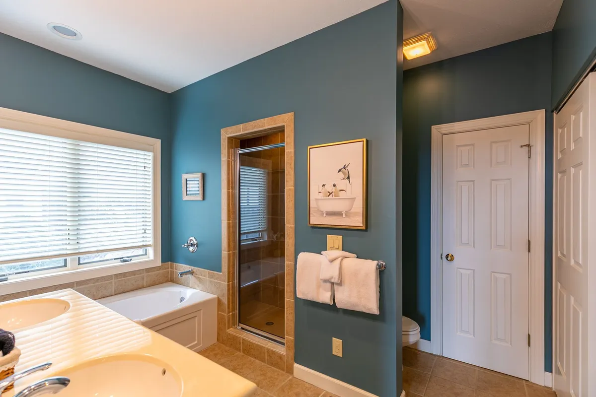 An elegant, serene bathroom featuring a double sink vanity, bathtub, shower enclosure, and large window. Fresh towels are neatly arranged and the space is bathed in natural light, conveying cleanliness and comfort.
